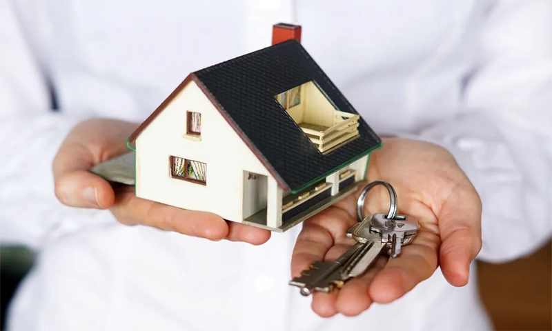 one hand holds a house model and the other holds a key