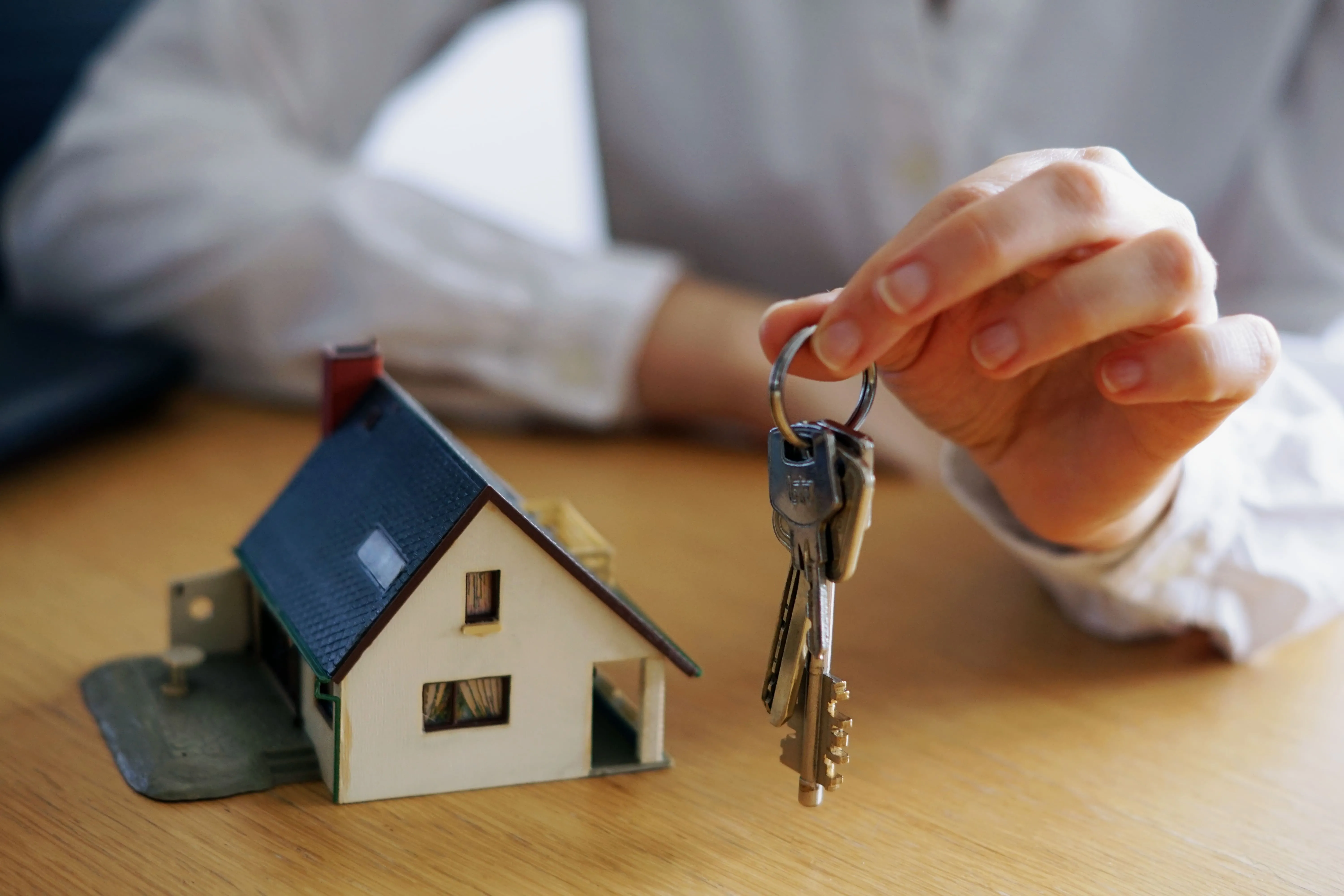 holding keys in one hand and a model of the house on the table